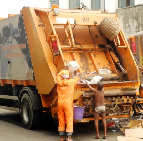 PIC.3. AN OFFICIAL OF LAGOS STATE WASTE MANAGEMENT AUTHORITY (LAWMA), AND A LITTLE BOY DISPOSING REFUSE INTO  LAWMA REFUSE VEHICLE IN LAGOS ON SUNDAY  (1/1/12).